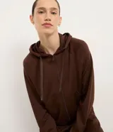 Campera deportiva Get Over confeccionada en mezcla de modal, poliéster y elastano, de color marrón oscuro. Presenta diseño con capucha ajustable con cordones estampados, cierre frontal completo por cremallera, mangas largas raglán con puños elásticos y bolsillos tipo canguro.