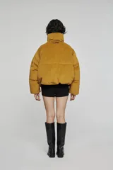 Chaqueta acolchada de corte corto y volumen amplio, color verde oscuro. Presenta cuello alto envolvente, cierre frontal con cremallera oculta, bolsillos laterales integrados y mangas de línea amplia.