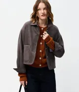 Campera corta de gamuza sintética color gris, con cuello camisero, bolsillos frontales aplicados, cierre de botones y mangas largas.