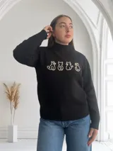 Sweater negro de tejido de punto con cuello alto y diseño de cuatro gatos blancos en el frente.