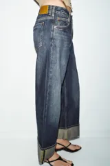 Jeans de tiro medio con corte relax fit y pernera holgada. Presenta diseño de cinco bolsillos, cierre frontal con cremallera y botón, y bajo con vuelta marcada.
