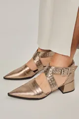 Zapato de cuero color peltre, con punta fina, tiras cruzadas con tachas y hebilla regulable.