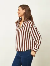 Blusa de color blanco con cuello en V y mangas largas con puños abotonados. Presenta un diseño de corte recto y holgado.