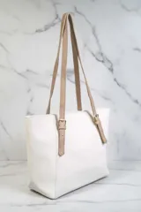 Bolso tipo tote bag de color blanco con textura granulada. Posee dos asas de hombro ajustables en color beige claro con hebillas metálicas.