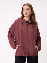 Campera rompevientos color bordó con cierre frontal, capucha con cordones ajustables y franjas laterales en tono más oscuro. Presenta puños elásticos y bolsillos frontales.