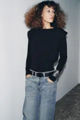 Jersey negro de punto, manga larga, con cuello redondo y detalle de pliegues o volados en la zona de los hombros.