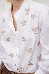 Camisa blanca de manga corta con cuello mao y volados, botones frontales y bordados de hojas y flores en color dorado.