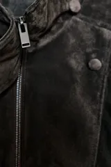 Cazadora tipo biker confeccionada en piel de ante 100%, con cuello subido, cierre frontal cruzado con cremallera y botones forrados. Presenta mangas largas con trabillas en los hombros, bolsillos de vivo en el delantero y bajo acabado en elástico.