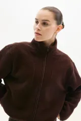 Campera deportiva de sherpa marrón con cuello elevado, cierre frontal y bolsillos laterales.