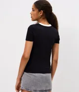 Remera de algodón con elastano, corte ajustado, cuello redondo y mangas cortas. Presenta un diseño en color negro con cuello blanco y vivos laterales blancos. Incluye estampa frontal del personaje Kuromi con detalles gráficos y texto.