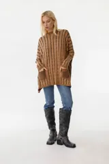 Sweater de punto color camel con diseño de trenzas verticales y acabado brillante. Presenta una silueta holgada tipo poncho, cuello redondo, mangas largas con puños ajustados y bolsillos frontales con detalle de etiqueta de cuero.