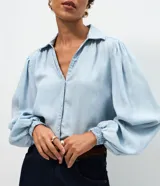 Camisa de denim liviano confeccionada en lyocell, con cuello camisero, cierre frontal de botones y mangas largas abullonadas con puños elásticos ajustados.