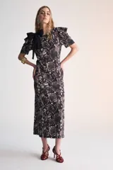Vestido midi de corte recto con estampado animal print en tonos marrones y negros. Tiene mangas cortas abullonadas, cuello redondo y un lazo negro decorativo en el hombro.