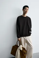 Sudadera negra de corte relaxed fit, confeccionada en tejido técnico interlock de algodón con elasticidad. Presenta cuello redondo, manga larga y una etiqueta aplicada en el bajo. Los acabados son en rib.