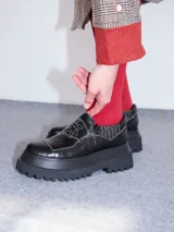 Mocasines de cuero negro con textura efecto cocodrilo, plataforma gruesa dentada, elásticos laterales y costuras blancas contrastantes con diseño en la solapa.