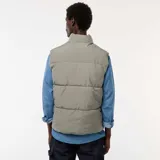 Chaleco acolchado puffer color gris, sin mangas, con cuello alto, cierre frontal de cremallera con solapa de botones a presión y bolsillos laterales amplios.