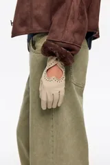 Guantes de piel ovina color beige, con diseño de recorte en forma de corazón en el dorso, decorado con pequeñas tachas metálicas alrededor y cierre de broche a presión en la muñeca.