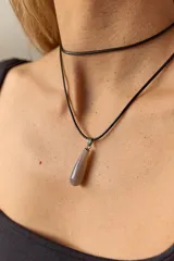 Gargantilla de cuero negro con dije de piedra blanca en forma de lágrima con engarce dorado.