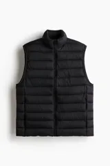 Chaleco acolchado negro de nylon con diseño guateado, cuello elevado, cierre frontal con protección para el mentón y bolsillos laterales. Corte entallado y diseño repelente al agua.