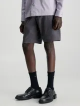 Shorts de corte slim color gris oscuro, confeccionados en sarga de algodón con elasticidad. Presentan talle medio, bragueta con cremallera, bolsillos laterales y de ojal en la parte trasera. Incluyen un cinturón con hebilla en forma de D.