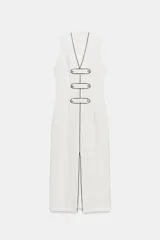 Vestido midi blanco sin mangas, con escote en V y costuras con ribetes negros a contraste. Cuenta con falsos botones decorativos en la parte delantera y una abertura central en el bajo.