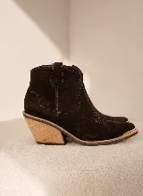 Bota corta estilo western confeccionada en gamuza color marrón oscuro, con taco de madera de diseño geométrico y puntera reforzada con detalle metálico.