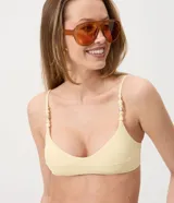Top de bikini bandeau color amarillo claro, confeccionado en microfibra texturada con tirantes finos regulables adornados con cuentas y caracolas.