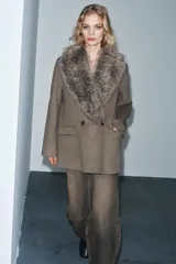 Chaqueta de corte recto confeccionada en mezcla de lana, color marrón topo. Presenta un cuello de solapa amplio con aplicación de pelo sintético desmontable, cierre frontal cruzado con botones y bolsillos laterales con solapa.