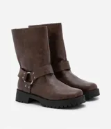 Bota marrón de cuero sintético, estilo biker, con caña media, puntera redonda, suela track y detalle de arnés con hebilla metálica.