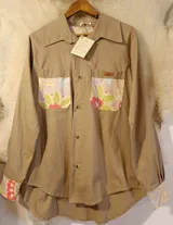 Sobre camisa beige de manga larga, con bolsillos en el pecho y detalles de tela guardamonte en los bolsillos y puños.