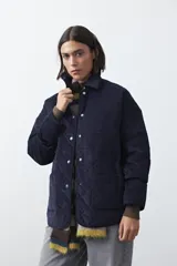 Campera capitoneada de algodón con diseño matelaseado, cuello camisero y cierre frontal con botones a presión. Presenta un corte relajado y bolsillos frontales.