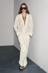 Camisa de algodón color crema o blanco roto, con textura de rayas verticales sutiles. Presenta cuello solapa, escote pico y manga larga.