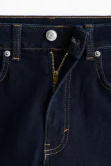 Jeans de cinco bolsillos en denim índigo oscuro, tiro alto, corte ajustado en la parte superior y pierna acampanada (flare) desde la rodilla. Presenta costuras en hilo contrastante color caramelo.