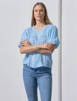 Blusa celeste de gasa con frunces en el frente, mangas cortas con puño elastizado, abertura central en la espalda con botón.