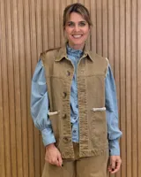 Chaleco de denim color marrón, confeccionado en 100% algodón, con bolsillos frontales amplios, cierre de botones y costuras decorativas bordadas en blanco en los bordes y los bolsillos.