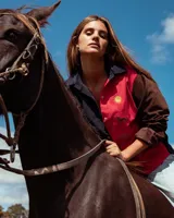 Camisa de pana de corte amplio con diseño color block, cuello camisero y mangas largas. Presenta bordados decorativos en el frente que incluyen un sol, un caballo y una bandera.