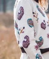 Sweater de punto color marfil con bordados artesanales en relieve de motivos paisley y florales en tonos morados, celestes y marrones. Posee cuello alto, puños y dobladillo en tono marrón oscuro.