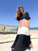 Vestido largo de diseño tricolor con bloques de color en negro, beige y crudo. Presenta escote en V, mangas cortas con volados y una falda amplia con cortes horizontales que crean un efecto escalonado.