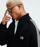 Campera deportiva de cuello alto con cierre frontal completo, mangas largas con rayas laterales blancas contrastantes y bolsillos laterales. Presenta un bordado pequeño en el pecho.