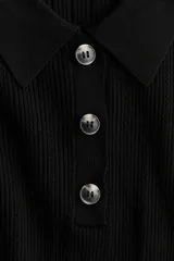 Top de punto pointelle acanalado en color negro, con cuello camisero, manga corta y tapeta con botones frontales.