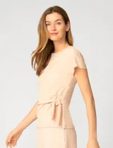 Remera de manga corta color beige, confeccionada en mezcla de modal, con cuello redondo y detalle de lazo lateral que genera un drapeado natural en la cintura.