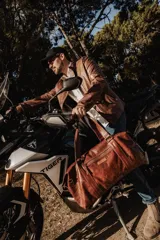 Bolso de cuero hecho a mano en color tostado, con diseño amplio y funcional. Presenta cierre superior, bolsillo frontal con cremallera, asas de mano reforzadas y una correa larga ajustable y desmontable.