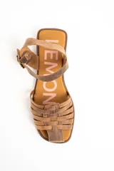 Sandalias cangrejeras de cuero color marrón, con diseño de tiras cruzadas en la parte delantera, suela plana y tira ajustable en el tobillo con hebilla metálica.