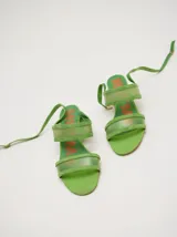 Sandalias de taco redondo de 6 cm, confeccionadas en gamuza verde con tiras frontales y de tobillo en material translúcido. Cuentan con cierre de pulsera al tobillo y plantilla de cuero.