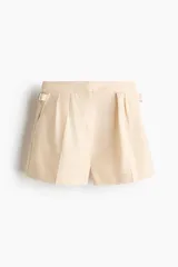 Short de mezcla de algodón y lino color beige, con pinzas delanteras, raya marcada al frente y ajuste con hebillas metálicas en los laterales.