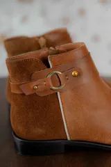 Botas cortas de cuero negro con paneles traseros de gamuza, cierre lateral y detalle de correa con hebilla metálica en el tobillo.