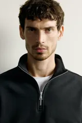 Sudadera negra de corte regular fit, con cuello subido, cierre frontal de cremallera corta y acabados en rib elástico en puños y cintura.