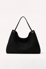 Cartera tipo hobo de gamuza negra, con diseño minimalista, asa única y detalles de argollas metálicas plateadas en los extremos.