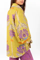Camisa de manga larga con cuello clásico y cierre frontal de botones, confeccionada en tejido de color verde lima con estampa floral en tonos morados y naranjas.