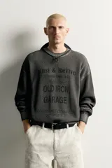 Sweater relaxed fit de algodón color gris con efecto lavado, cuello redondo, manga larga y diseño de textos estampados a contraste en el frente.
